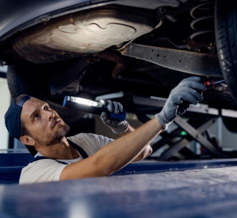 auto-mechanic-examining-undercarriage-of-car-with-flashlight-in-repair-shop